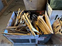 Box filled with multiple natural wood shirt and pants hangers with metal hooks seen inside a Sharp microwave box.