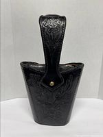 Front view of vintage 1960s black hand tooled leather handbag showing floral design and handle with embossed floral tooling.