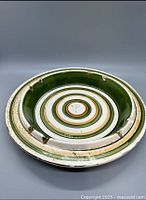 Top-down view of ceramic ashtray showing worn surface, concentric circle pattern in green, white, brown, and multiple cigarette rests around the rim.