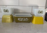 Front view of five Pyrex refrigerator dishes showing floral pattern and solid color bases.