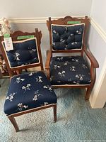 Two wooden chairs placed side by side with blue floral tufted cushions on seats and backs, showing style and condition.