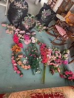 Wide view of the three bags filled with assorted artificial flowers along with various floral arrangements laid on the floor including numerous pink, red, and orange flowers