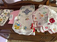 Vintage cloth napkins and doilies displayed on wooden surface, various embroidered and printed patterns visible