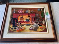 Full view of framed needlepoint showing colonial home interior with rocking chair, fireplace, spinning wheel, and hearth details.