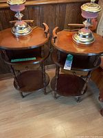 Pair of wooden end tables side by side with lamps on top, showing rounded rectangular tops with side handles, drawers, and lower shelves.