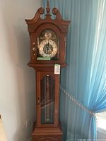 Full view of handcrafted wooden grandmother clock with carved wooden hood and glass front door.