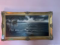 Front view of L Pichler coastal seascape painting in an ornate gold frame against a pink wall.