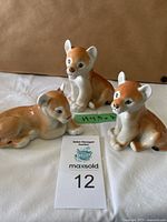 Set of three vintage baby lion porcelain figurines, arranged with the tallest in the back and two smaller lions in front on a white cloth.