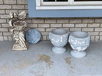 Four pieces of outdoor decor on porch step include two urn-style planters, one bird nest planter sculpture with two birds, and a circular wall plaque.