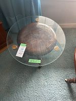 Glass top showing round clear glass surface sitting on the wooden piano stool seat, with visible wear on wood beneath.
