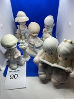 Five Precious Moments porcelain figurines displayed on a blue background, showcasing the different poses including reading and holding birds.