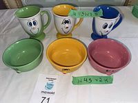 Set of three bowls and three matching cups with unique smiley faces in green, yellow, and pink colors for bowls and green, yellow, blue handles for cups