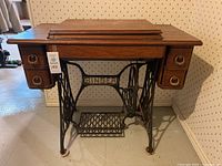 Front view of the Singer sewing machine table showing wooden top, two drawers with ring handles, and cast iron treadle base with 'SINGER' nameplate.