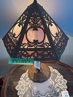 Front view of lamp showing pink swirl glass panels and dark metal filigree shade on round metal base.