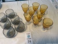 Full view of the 6 amber yellow Berwick Boopie cordial glasses and 4 gray smoke-colored lowball glasses on a white surface.
