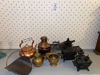 Overview of the lot showing all items including bronze and brass kettles, mini cast iron stoves, ship port light, pestle and mortar, and a metal bucket.