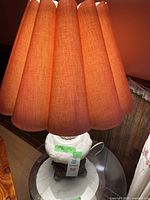 Full view of lamp showing pleated pink fabric shade and ornate white ceramic base with brass accents and crystals hanging beneath shade.