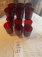 Twelve red glass goblets grouped together in three rows of four on a white tablecloth.