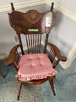 Full view of vintage wooden rocking chair with pink seat cushion, showing carved backrest and spindled arms.