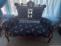 Front view of vintage wooden settee with blue floral fabric upholstery and carved backrest.