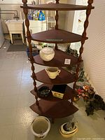 Full view of the vintage wooden corner stand with five tiers and various decorative items displayed on shelves and floor around it, showing shape, wood finish, and items included.