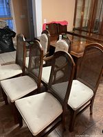 Side view showing 4 dining chairs with woven cane backs and cream fabric seats arranged in rows next to a dining table.