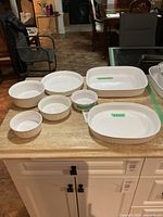 7 white glass Corning French cooking dishes arranged on a countertop, showing all pieces included in the set