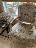 Armchair showing floral upholstery, white-washed wood frame, and curved armrests with padded fabric covering.