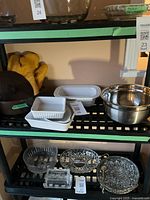 Shelf with brown Cousances roasting dish, white ceramic baking dishes (square and rectangular), yellow oven mitts, and stainless steel mixing bowl.