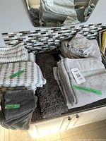 Overview of multiple folded bath, hand, and face towels with a plush dark gray bathmat underneath on a white countertop with tiled backsplash.