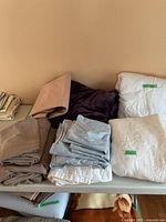 Assortment of folded bedding items including blankets, sheets, and comforters in different colors on a table.