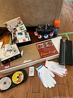 Full view showing quilling art supplies kit, Chris Craft model boat kit box, craft glues, spray adhesive, two pairs of white gloves with colored trim, and a black paper cutter on the floor.