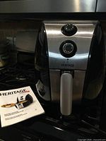Front view of Heritage electric air fryer showing temperature and timer dials, handle, and stainless steel finish.