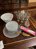 Overview of lot showing gold plated cake server, glasses, white bowl, textured clear glass dishes and platter, box and candlestick with red candle.