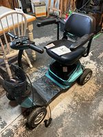 Full side view of teal and black 4-wheel scooter showing seat, armrests, floorboard and tires