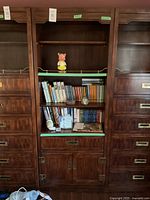 Full view of the large wall unit showing upper open shelves with books and figurines, middle drawer, and lower cupboard with doors and brass handles.