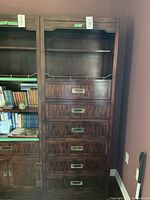 Full view of the dark wood wall unit showing six drawers with inset brass handles and two open shelves above, against a brown wall corner.
