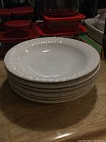 Stack of six white soup bowls with a subtle grooved raised edge pattern.