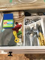 Drawer with kitchen towels, small brushes, cutlery with bone colored handles, and other utensils.