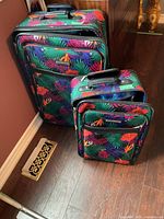 Two floral pattern matching soft luggage pieces standing next to each other on the floor.