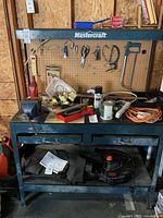 Front view of Mastercraft workbench with items on top, pegboard back, two drawers below and bottom shelf