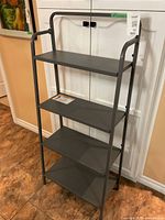 Front view of metal shelf unit showing four shelves and open tubular frame design in dark gray metal.