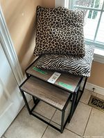 Nesting tables stacked with two throw pillows on top showing animal print covers and wear.