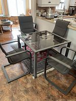 Square metal frame table with clear glass top and four chairs around it