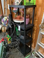 Black four-tier plastic shelving unit with black metal brackets for wall mounting; shelves contain various items not included in lot.