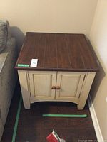 Front view of wood side table with brown top and painted cream sides, showing two doors with round wooden knobs.