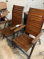 Two reclining patio chairs with metal frames and wooden slats for seat, back, and armrests.
