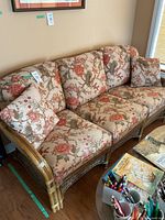 Front side view of wicker and rattan couch with floral cushions and pillows on wooden floor near wall.