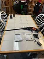 Full view of Worx cordless power cleaner gun with wand, battery, charger, and manuals on table.