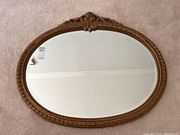 Front view of the oval mirror showing full frame with ornate top detail and gold plaster finish